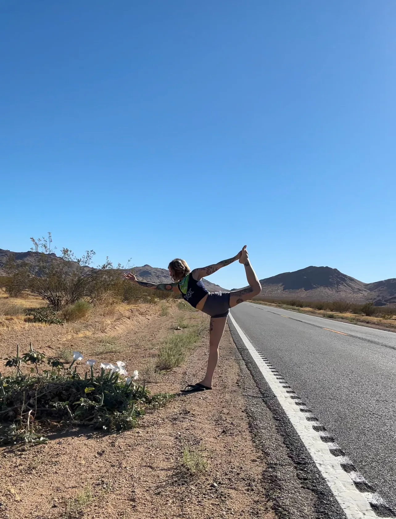 LeeAnna in dancer's pose on a desert roadside with mountains behind